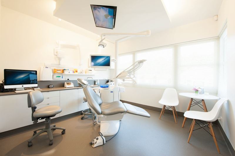 A doM treatment room: a modern dental chair beside large windows, with a screen on the ceiling for patients to watch.